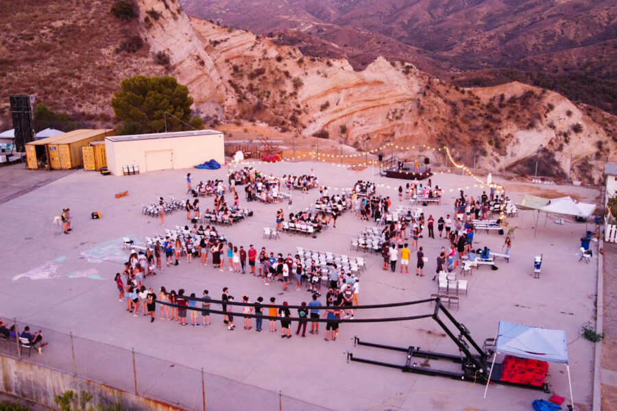 aerial view of a number of groups of teens on a wide open court outside at dusk.