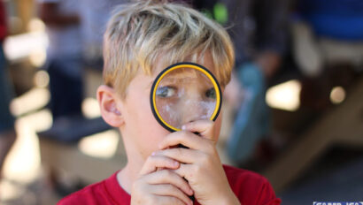 boy looking through a magnifying glass facing the camera.