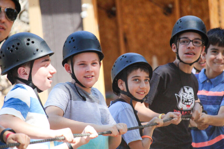 boys wearing helmets while holding onto a rope.