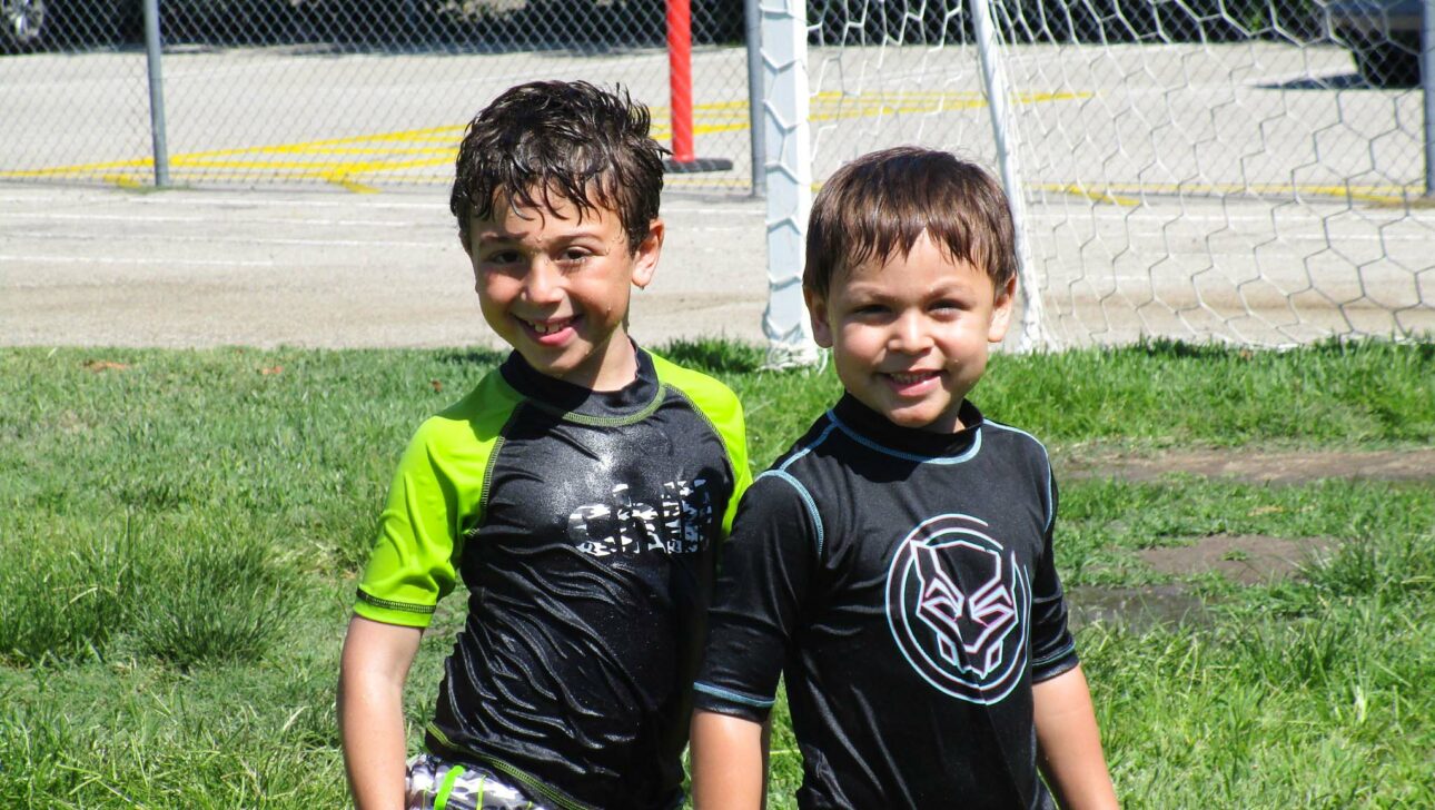 two boys in wetsuits on a soccer field.