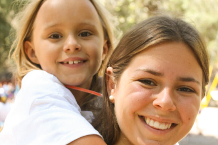 camp counselor giving a young girl a piggyback ride.