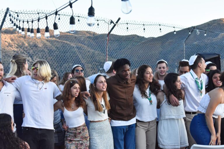 group of teens in white leaning on each other and singing.