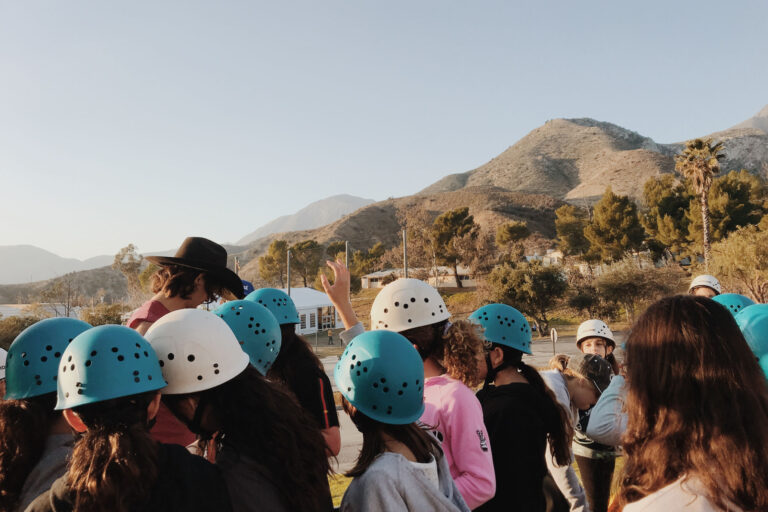 group of kids wearing blue and white climbing helmets outside.