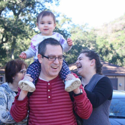 baby carried on a dads shoulders with two other family members.