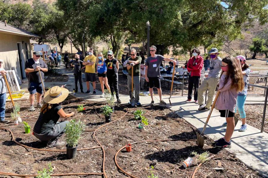 women kneeling in a garden patch and teaching surrounding families about gardening.