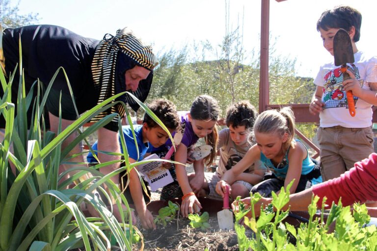 kids gardening with a man in a headdress.