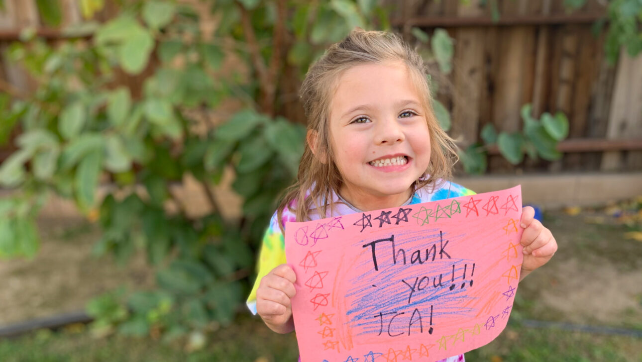 young girl smiling and holding a sign that says thank you jca.