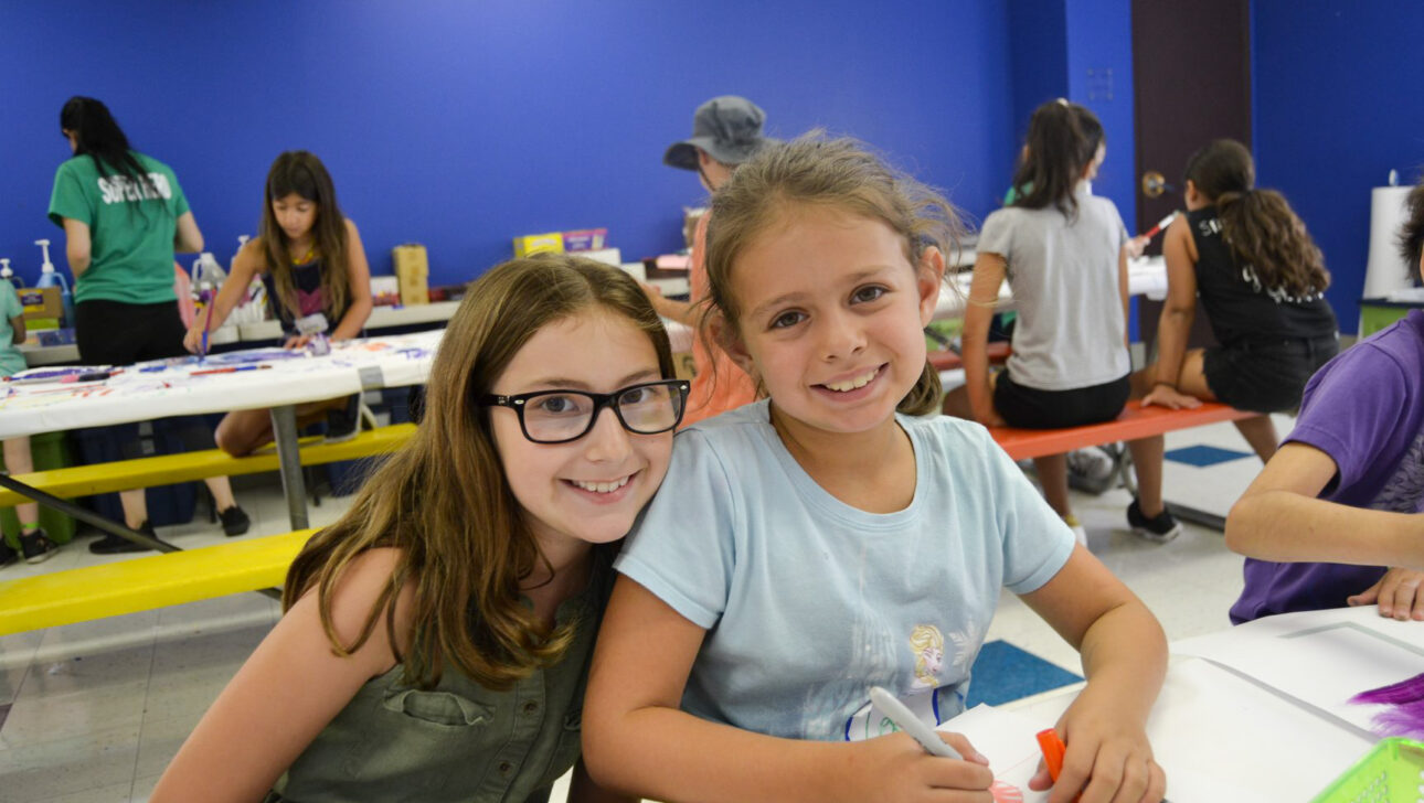 two girls smiling while working on art in a classroom.