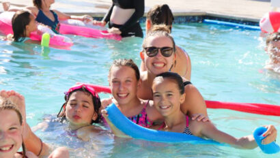 group of kids smiling and swimming in a pool with a camp counselor.
