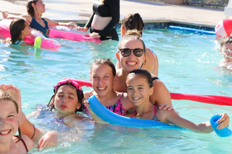 group of kids smiling and swimming in a pool with a camp counselor.