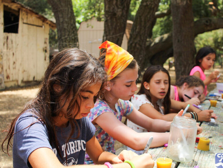 girls writing at a picnic table outside.