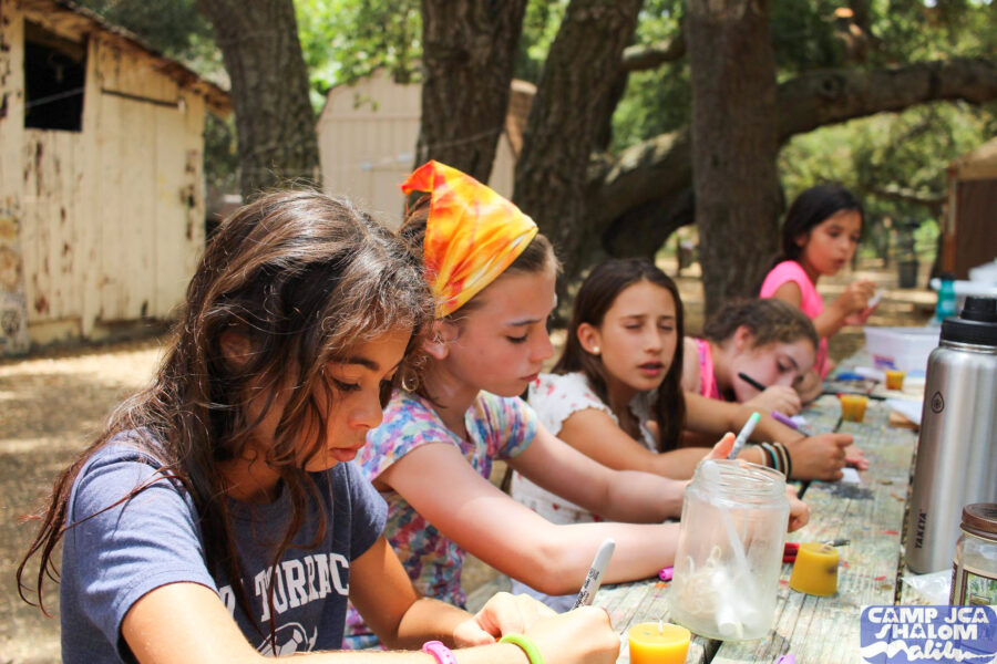 girls writing at a picnic table outside.