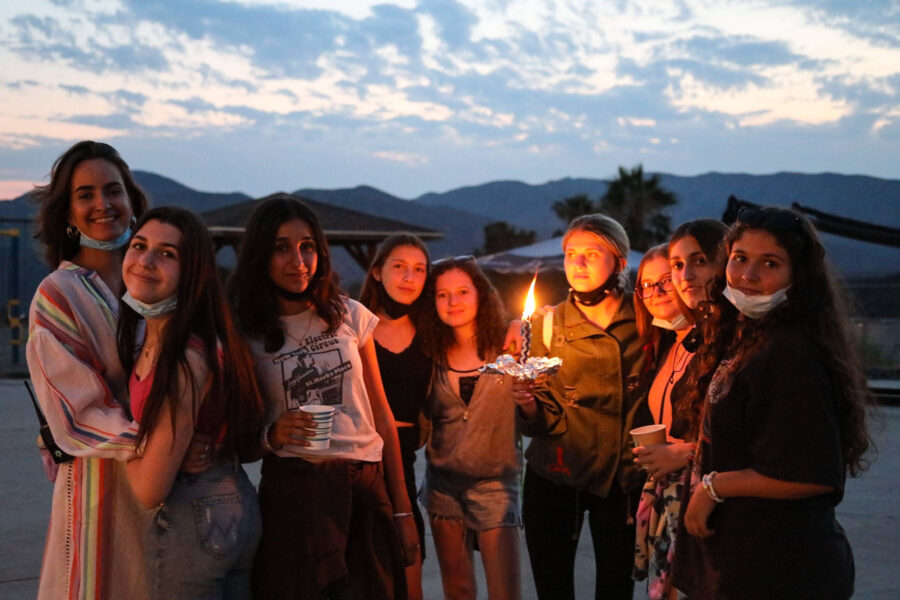 group of friends outside at dusk huddled around a camera.