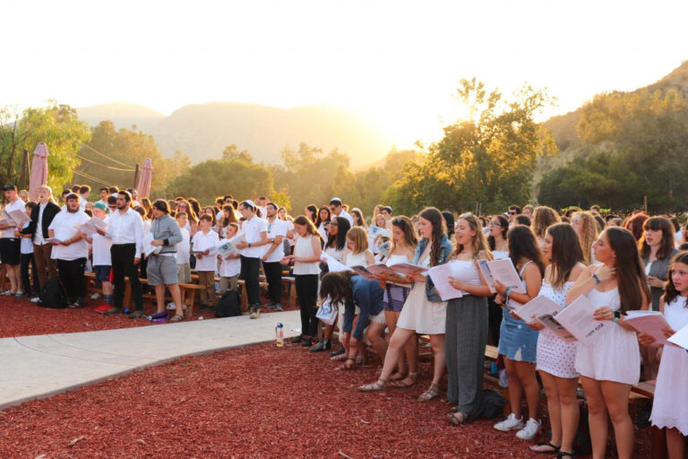group of teens in white singing together outside.