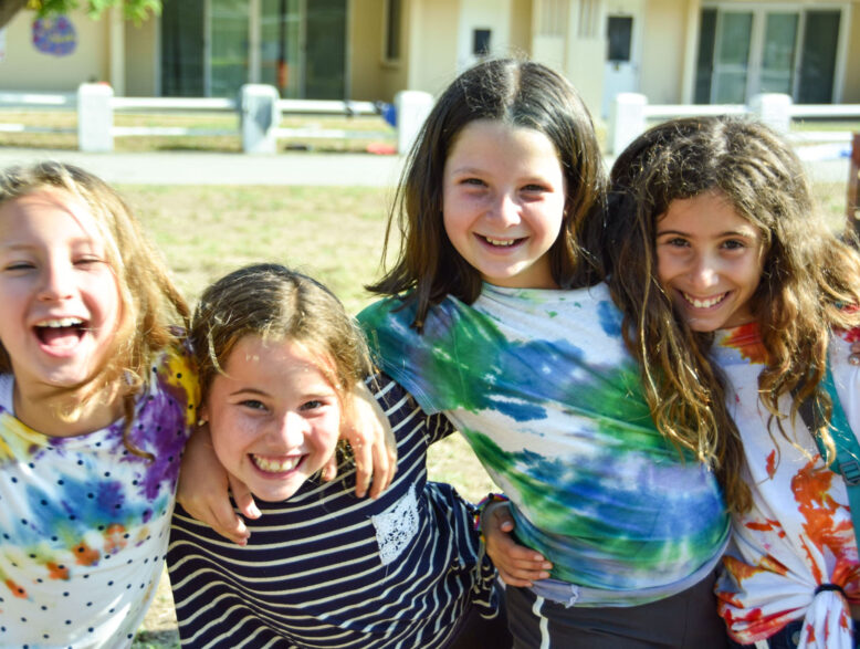 four smiling girls in tie dye shirts.