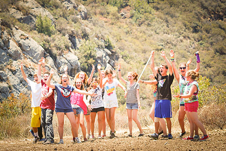 group of kids holding their hands in the air while hiking.