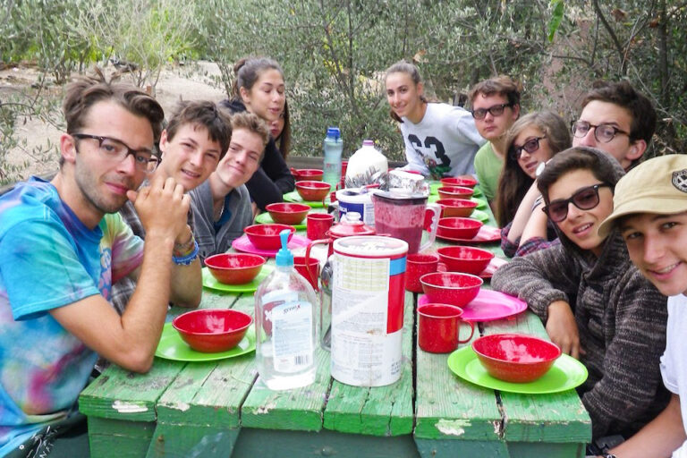 kids and teens sitting at a green picnic table outside.