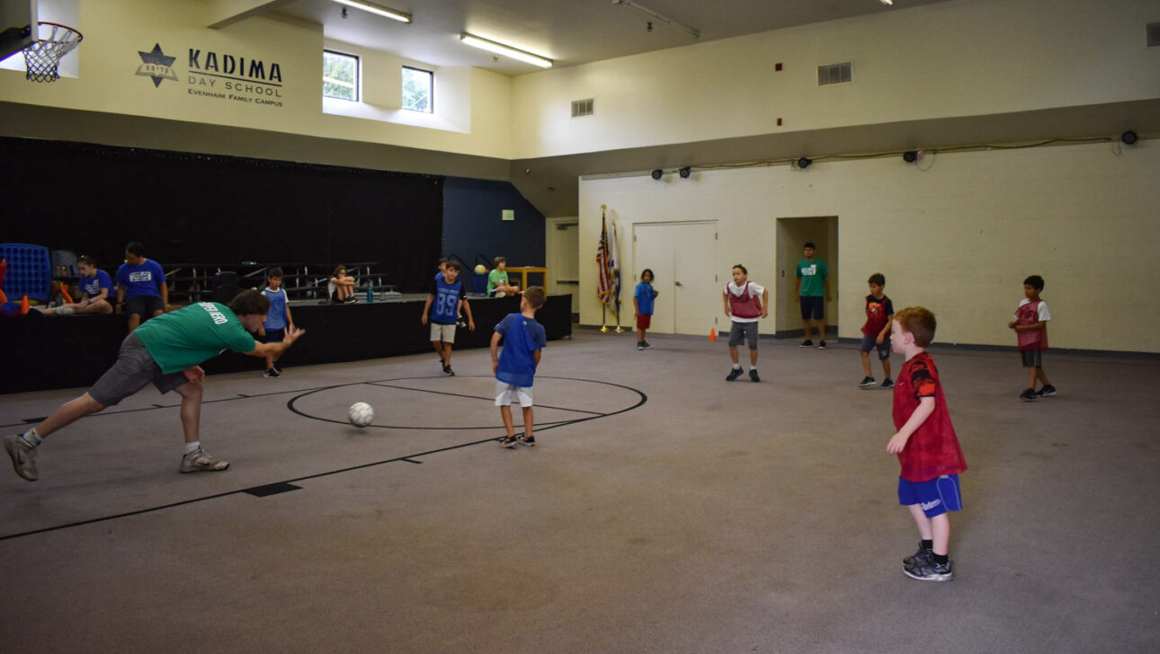 kids playing kickball indoors with a camp counselor.