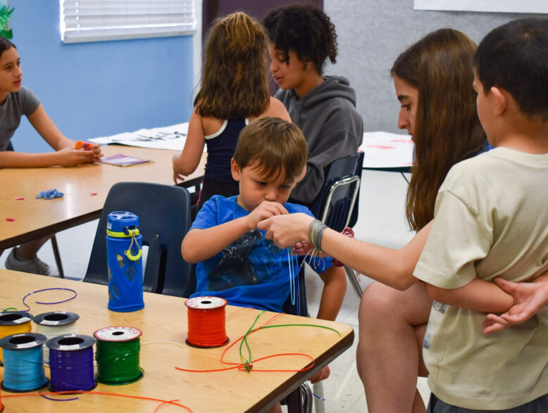 kids making lanyards with a camp counselor.