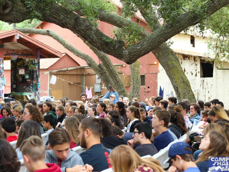 kids sitting outside on benches listening to a speaker.