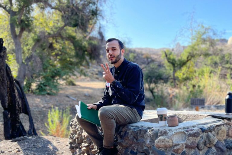 man teaching something outside while sitting on a stone wall.