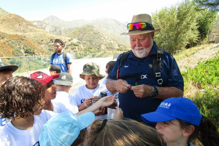 man on a nature field trip showing something to a group of kids.