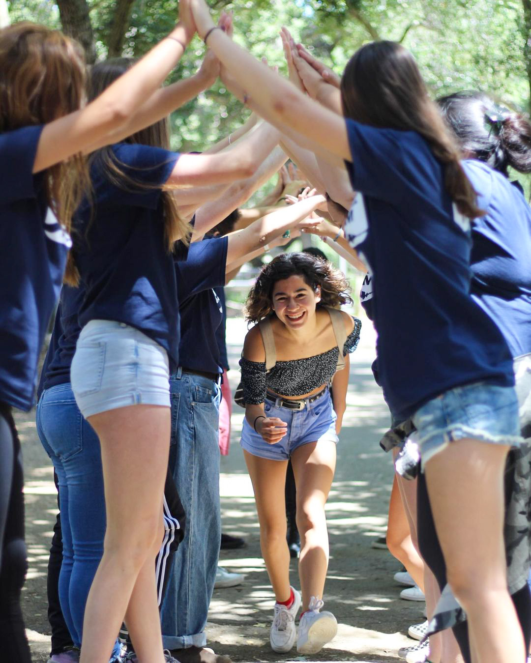 teen girl running through the arched arms of a group of camp counselors.