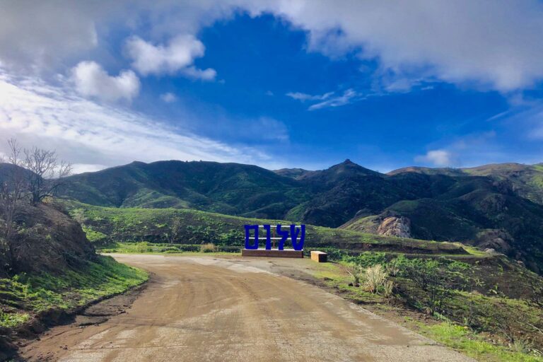 blue sign on a dirt road in green mountains.