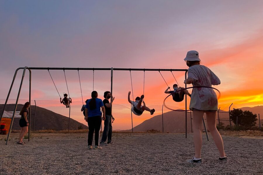 kids swinging on a swingset in front of an orange sky.