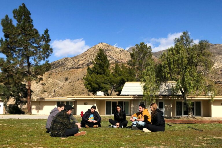 group of teens sitting on a lawn outside in front of a building.