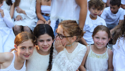 girl telling a secret to another in a group of kids.