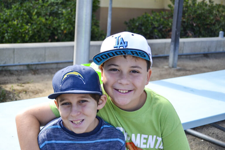 two boys smiling for the camera in ball caps.
