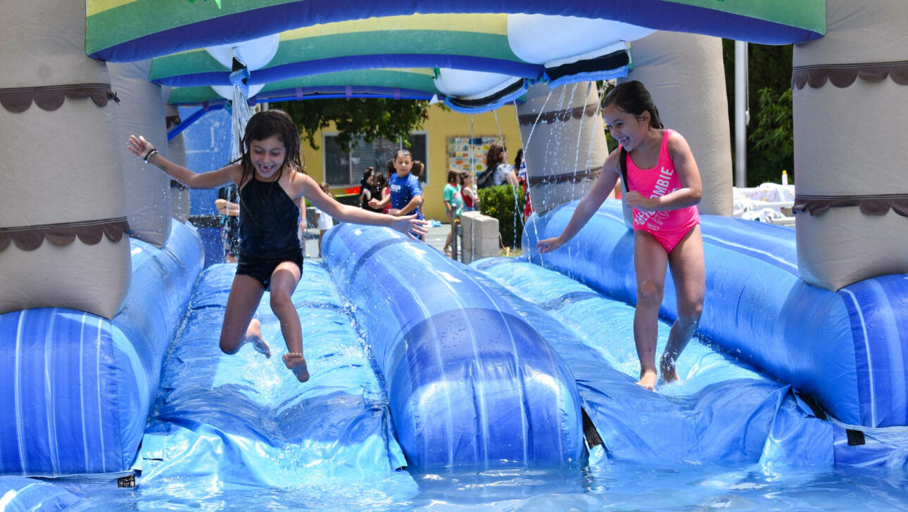 two girls running down an inflatable water slide.