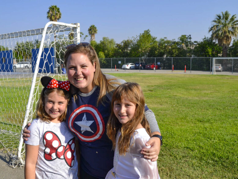 two girls smiling in front of a woman on a soccer field.