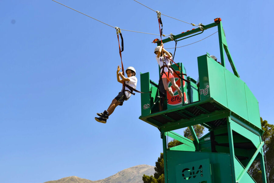 two boys jumping off a platform on a zipline.